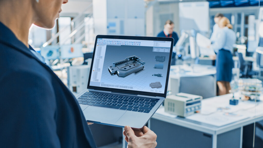 stylish female industrial robotics engineer uses laptop computer with cad software and to manipulate and program robot arm for lifting, moving objects technology research facility for machine learning